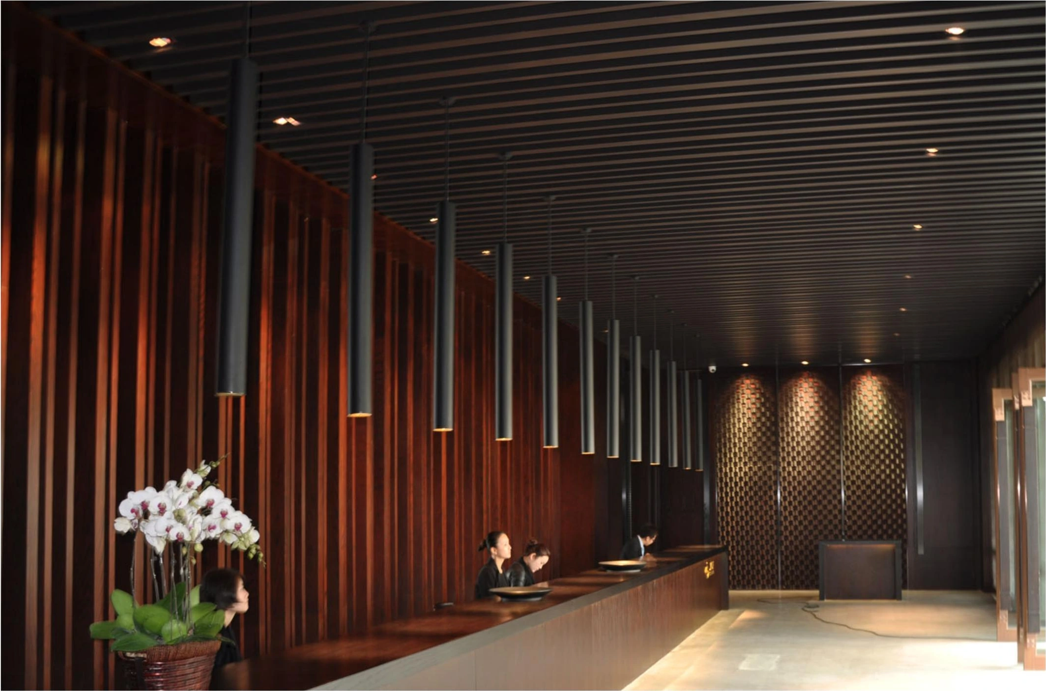 Wood-look vertical wall slats and dark linear ceiling in a Chongqing mixed-use lobby