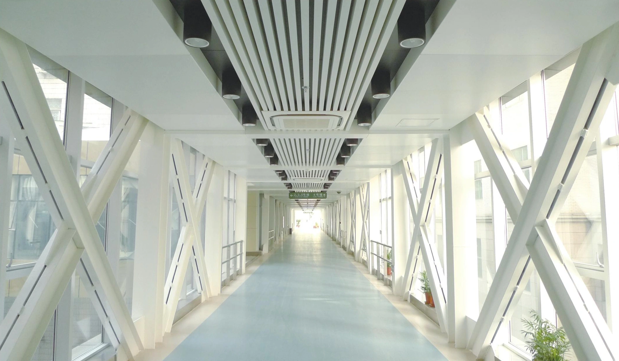Linear metal ceiling above an enclosed hospital bridge with diagonal side braces in Shenyang