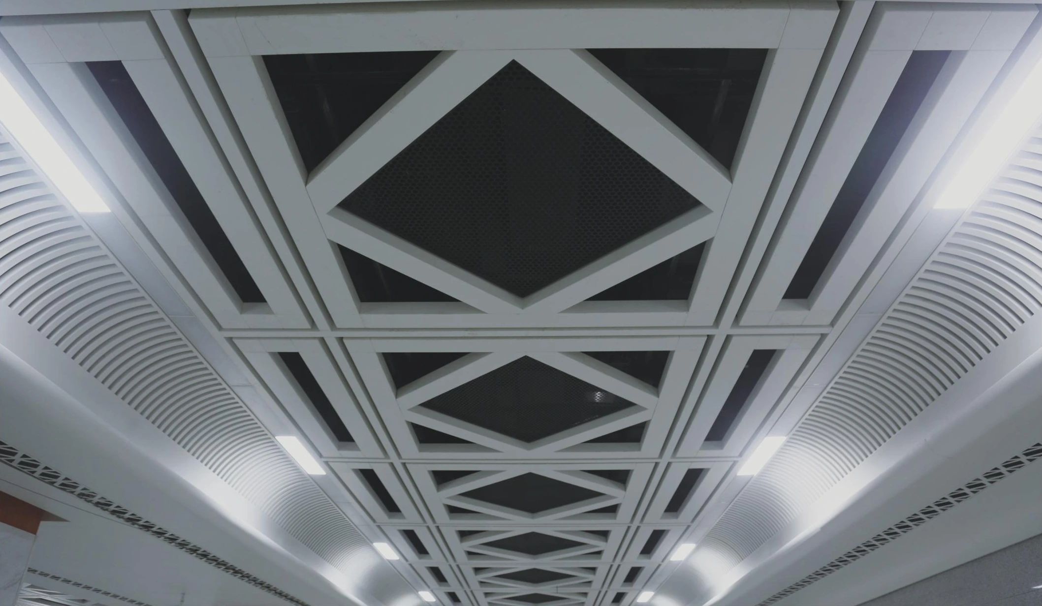 Diamond-pattern aluminum ceiling above a Wuhan metro platform corridor