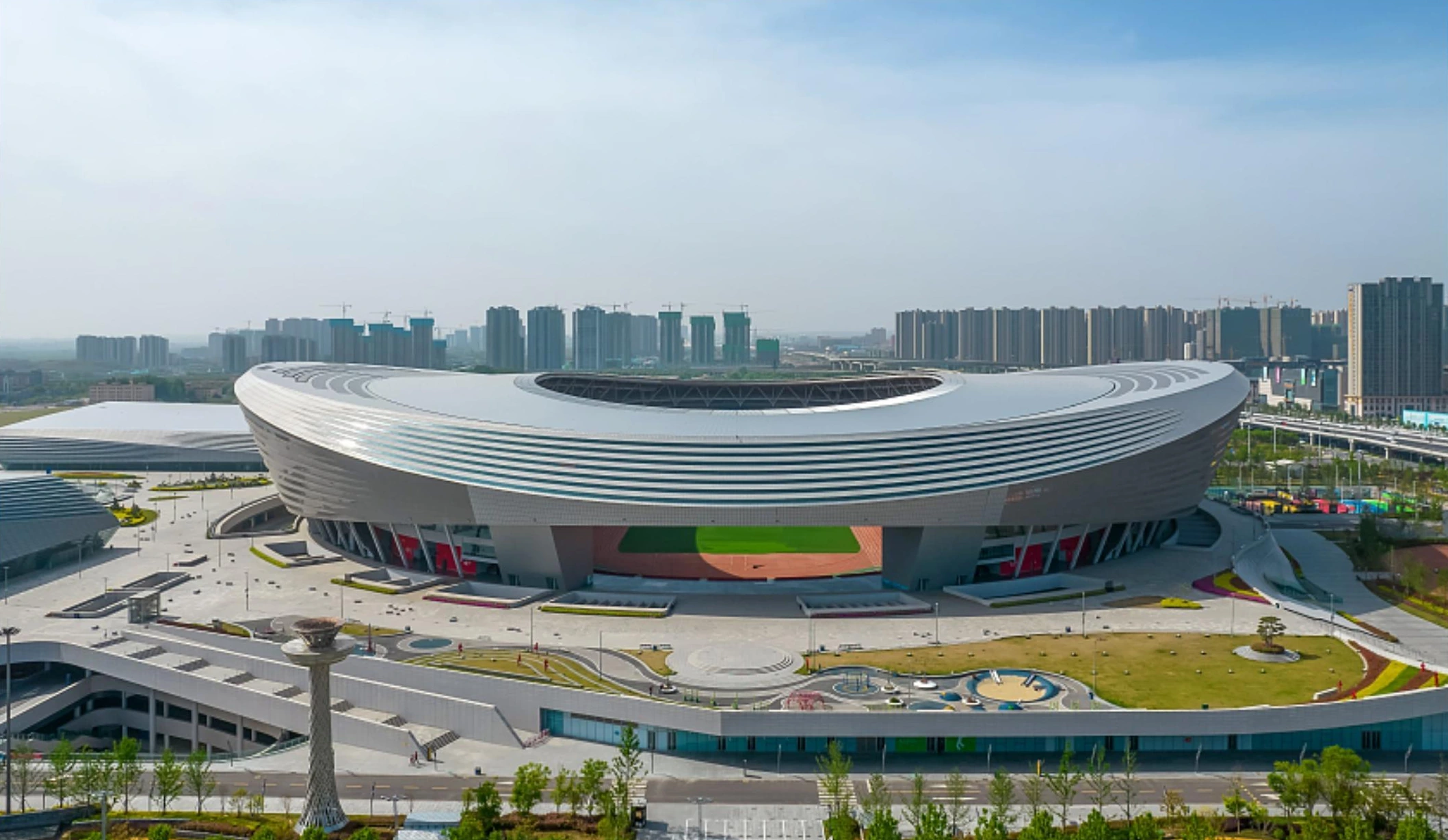 Aerial view of an oval sports venue with horizontal metal roof bands in Zhengzhou
